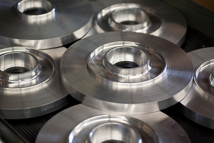 a collection of metallic round parts with a central hole and raised concentric rings. The reflective surface indicates that the parts are either polished or have a machined finish. These components might be used in mechanical assemblies, possibly as flanges or bearings, where a shaft or pipe would pass through the central hole. The parts are manufactured with precision and have a high-quality finish, which is essential for components that are likely to be part of a larger machine or system requiring tight tolerances and smooth surfaces to function correctly. The image conveys a sense of industrial craftsmanship and the capabilities of modern manufacturing technologies.